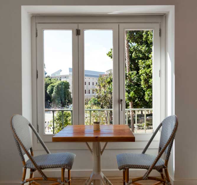 Dining nook with wooden table and chairs facing large white-framed Casement Windows Atlanta, overlooking greenery and allowing abundant natural light into the home.