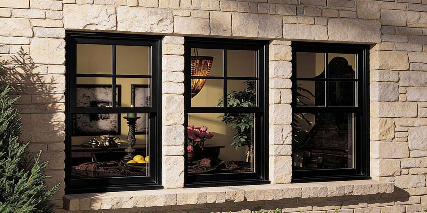 Stone exterior wall featuring three black-framed Double Hung Windows Atlanta, showcasing classic grid design, balanced proportions, and elegant residential window installation.