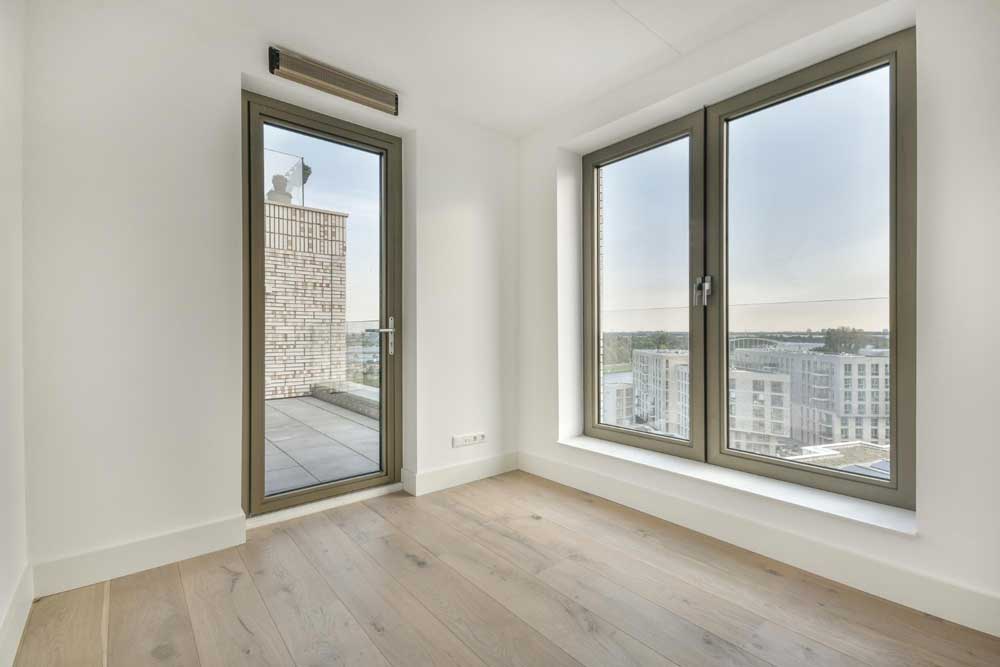 Modern empty room with large glass window and door leading to balcony, showcasing professional Window Replacement Calhoun County for contemporary residential window installations